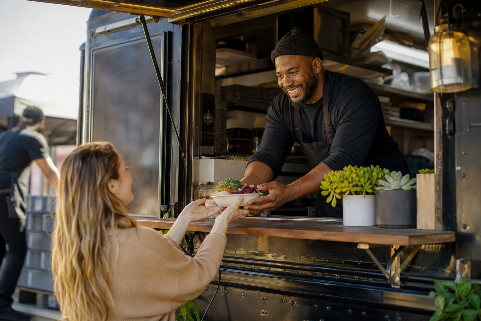 Food truck operator serving customers at a festival with mobile kitchen prep visible and morning natural light